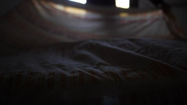 Adult man tidies the bed with a cotton sheet. Authentic modern and real life scene.
