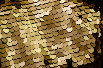 Gold fabric with round sequins. Elegant holiday background in gold color. Scaly pattern.