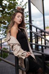 beautiful slim young brunette in fashionable trench coat and black dress walking near stairs. autumn, yellow leaves. .