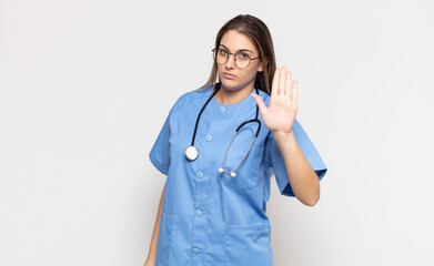 young blonde woman looking serious, stern, displeased and angry showing open palm making stop...