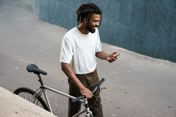 African american guy using cellphone while walking with bicycle