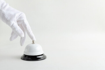 Butler wearing white glove and ringing service bell, bright background.Empty space