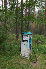 An old petrol pump for fueling a car is abandoned in a pine forest. Travel to the provinces of Russia in the summer.