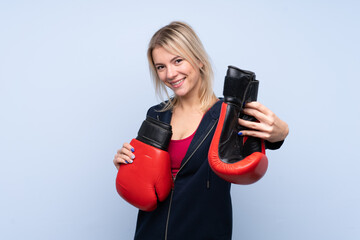 Young sport blonde woman over isolated blue background with boxing gloves