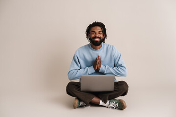 Happy african american guy sitting with laptop on floor