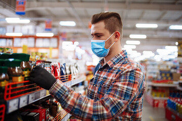 Young man is choosing goods at a supermarket wearing a medical sterile mask during the coronavirus pandemic quarantine. Healthcare, hygiene, covid-19 and home sanitizing concept.