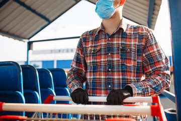 Young man stands outside the supermarket with the trolley wearing sterile medical mask and gloves...