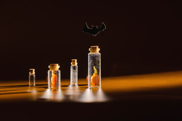 A set of glass bottles with liquid and mini pumpkins on a dark orange background with a contour...