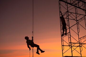 The worker silhouette is abseiling. To do construction work at the site