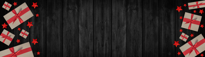 Fototapeta premium Festive Christmas / Advent background banner panorama - Top view / above view from gift boxes with red ribbon and stars, on rustic black wooden boards, wood table texture