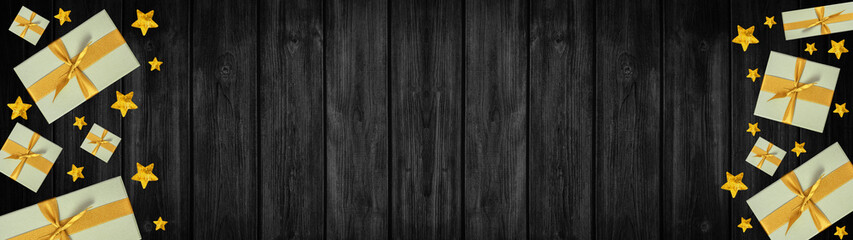 Fototapeta premium Festive Christmas / Advent background banner panorama - Top view / above view from yellow golden gift boxes with ribbon and stars, on rustic black wooden boards, wood table texture
