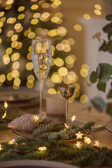 A glass of champagne in the background of the Christmas table and the lights of the Christmas tree