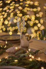 A glass of champagne in the background of the Christmas table and the lights of the Christmas tree