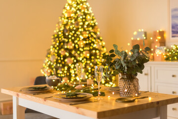 A glass of champagne in the background of the Christmas table and the lights of the Christmas tree