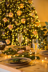 A glass of champagne in the background of the Christmas table and the lights of the Christmas tree