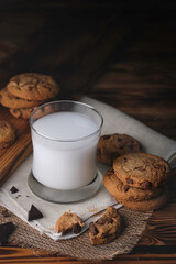 Glass of milk with appetizing delicious sweet homemade chocolate chip on dark vintage wooden table. Tasty dessert for breakfast with copy space for your advertising content