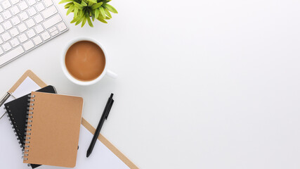 Top view white wooden workspace office desk with computer and office supplies. Flat lay work table with blank notebook, keyboard, green leaf and coffee cup. Copy space for your advertising content.