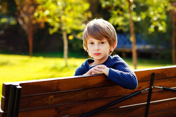 A charming red-haired boy sits on a Park bench and looks at the camera.