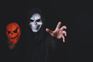 Horror devil costume with spooky pumpkin skull in black dressed for halloween carnival. Devil cosplay holding ghost mask and raise hand with blank copy space for your advertising content.
