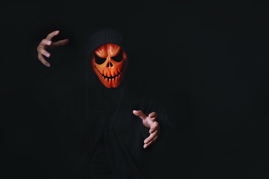 Horror devil costume with spooky pumpkin skull in black dressed for halloween carnival. Devil cosplay in ghost mask and raise hand with blank copy space for your advertising content.
