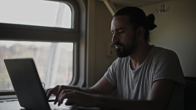 The man on the train is working on the computer. Prints text on laptop keyboard.