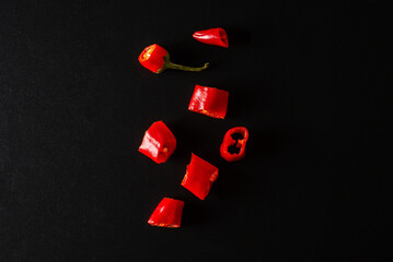 Fresh chili peppers, cut into pieces, lie on a black background.