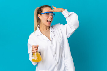 Young scientific woman isolated on blue background doing surprise gesture while looking to the side