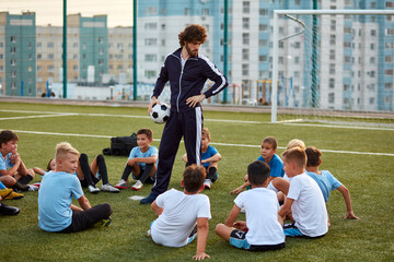 friendly kid boys have rest with trainer during football competition, confident male trainer give...