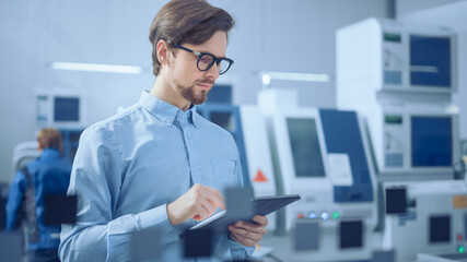 Modern Factory: Industrial Engineer Standing in Facility Workshop, Using Digital Computer, Inspecting and Monitoring Assembly Line Fucntioning. Functional Manufactory with CNC Machinery