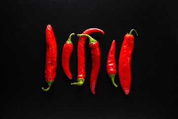 Fresh chili peppers of red color evenly arranged on a black background.