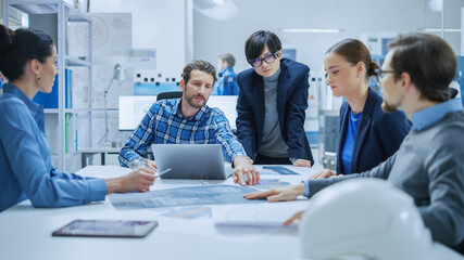 Modern Factory Office Meeting Room: Multi Ethnic and Diverse Team of Engineers, Managers and Investors Talking Sitting at Conference Table, Analyzing Blueprints. High-Tech Manufactory Optimization