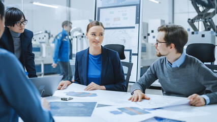 Modern Factory Office Meeting Room: Young Female Specialist Reports to Diverse Team of Engineers, Managers, Businesspeople and Investors Sitting at the Conference Table Analyzing Blueprints
