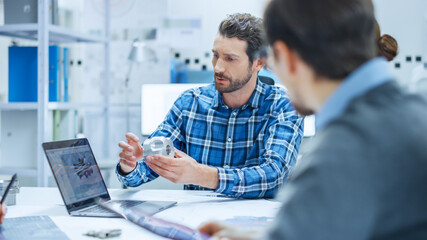 Modern Factory Office Meeting Room: Multi-Ethnic and Diverse Team of Engineers, Managers and Investors Talking Sitting at Conference Table, Analyzing Blueprints, Showing Information on Laptop Computer