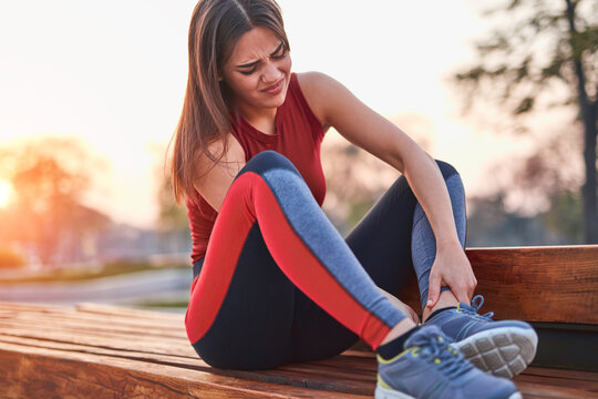 Young sportswoman having pain / injury during exercise and jogging in the park.