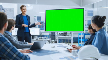 Modern Industrial Factory Meeting: Confident Female Engineer Uses Interactive Green Mock-up Screen...
