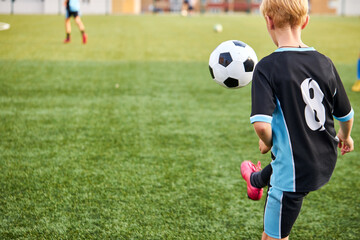 young caucasian kid boy with soccer ball is in motion on green grass background, boy in uniform is in action, run and play with ball