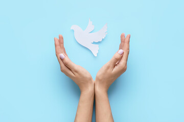 Female hands with paper dove on color background. International Day of Peace