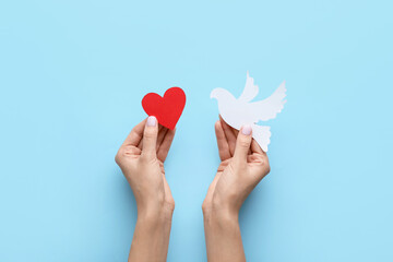 Female hands with paper dove and heart on color background. International Day of Peace