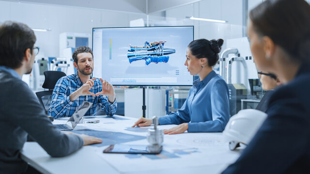 Modern Factory Office Meeting Room: Diverse Team of Engineers, Managers and Investors Talking at Conference Table, Use Interactive TV, Analyze Sustainable Energy Engine Blueprints. High-Tech Facility - Powered by Adobe