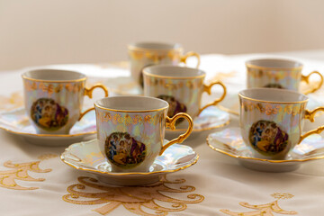 A set of six festive, decorated, painted cups built on a gold embroidered Christmas tablecloth.