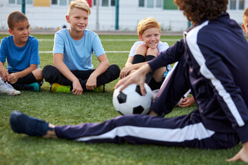 Obraz na płótnie Canvas friendly kid boys have rest with trainer during football competition, confident male trainer give advice, explain and have talk with sportive boys, in stadium