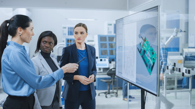 All-Female Team: Concept Developer, Computer Engineer and Manager Use Digital Interactive Whiteboard That Shows 3D Printed Circuit Board Concept. Developers Find Problem Solution. Factory Meeting Room