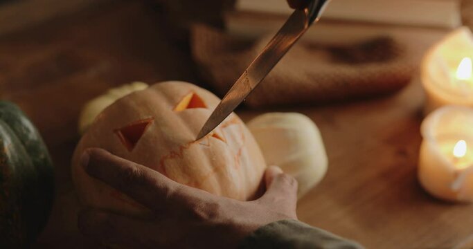 Man carving Jack o' Lantern with a knife in a moody table lit by candles, medium shot, tilt camera movement, 4k, cinematic