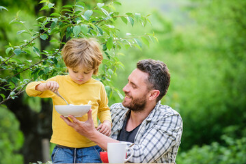 Fototapeta premium Best weekend ever. healthy food and dieting. Dairy products. family dinner time. Morning breakfast. Vegetarian diet. happy fathers day. Little boy with dad eat cereal. father and son eating outdoor