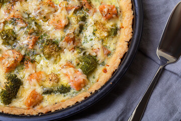Quiche (open pie) with trout, broccoli and cheese. Homemade unsweetened pastries, traditional pie. Close-up.