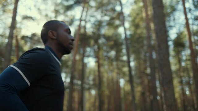 Young fit African American male jogging on a forest road.