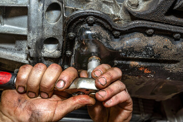 The car mechanic bolts a new screw with a copper washer to the oil sump, in a diesel engine.