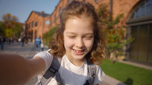 Cute schoolgirl taking selfie or having video call outside school