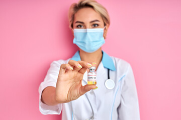 young caucasian female doctor holding small vaccine bottle in hand, medical injection, treatment from epidemic covid-19