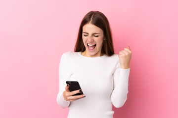Fototapeta premium Young woman over isolated pink background with phone in victory position